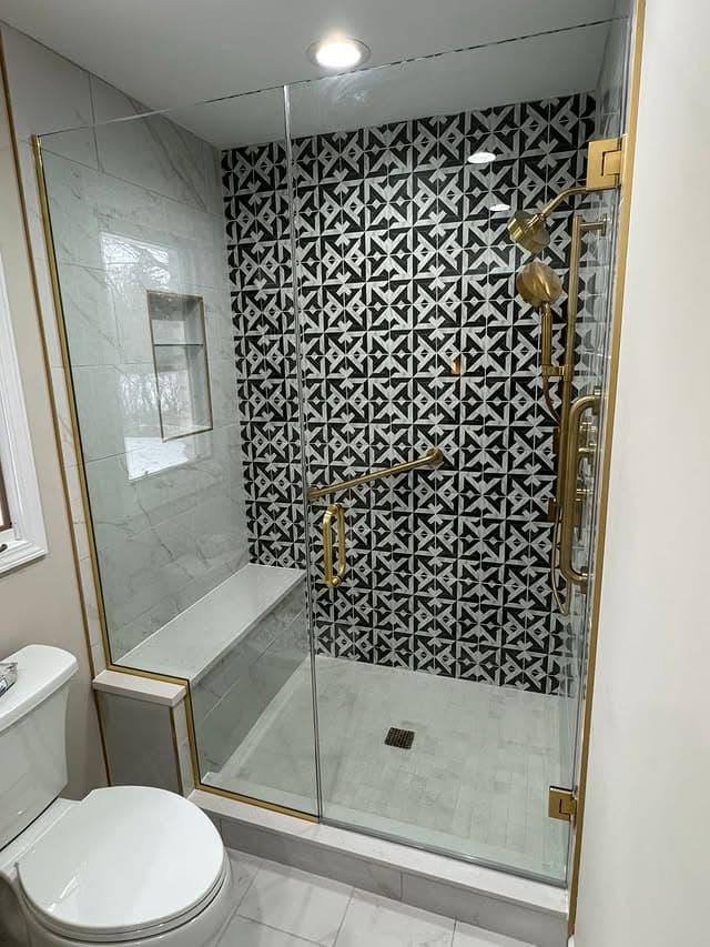 Glass shower with black and white geometric tile and brass fixtures